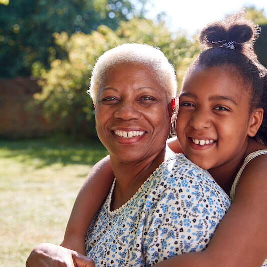 Senior black woman and granddaughter sit embracing outside